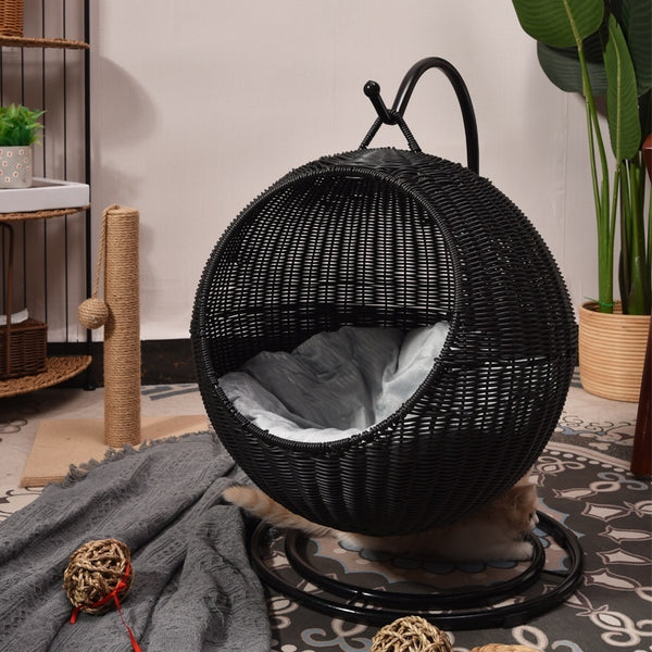 Black woven cat hammock with a soft cushion inside, placed on a patterned rug.
