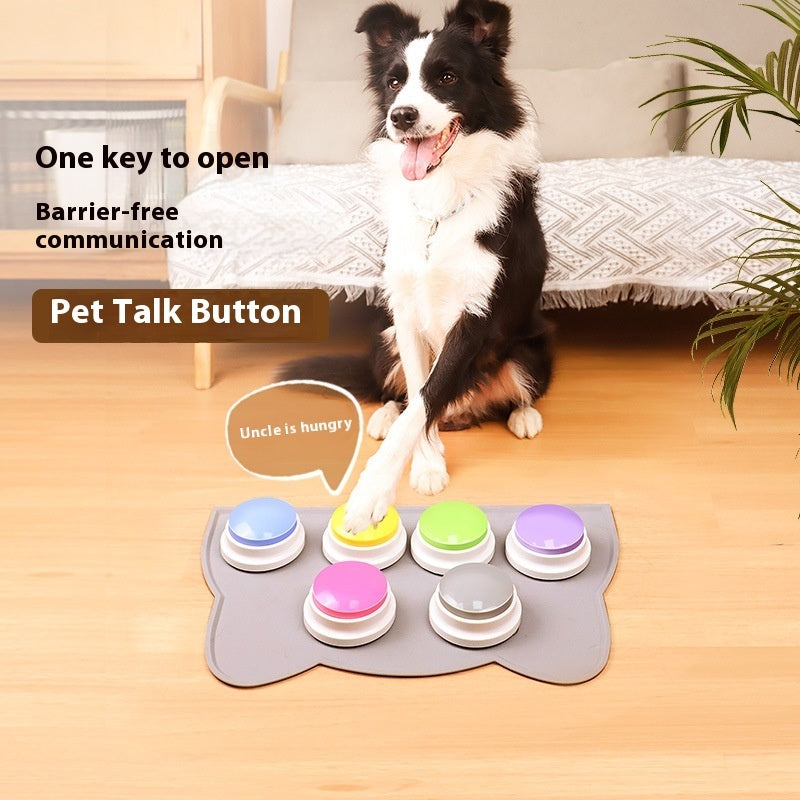 Dog interacting with a pet talk button device on a wooden floor.