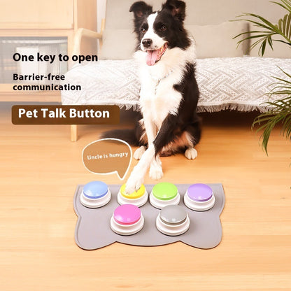 Dog interacting with a pet talk button device on a wooden floor.