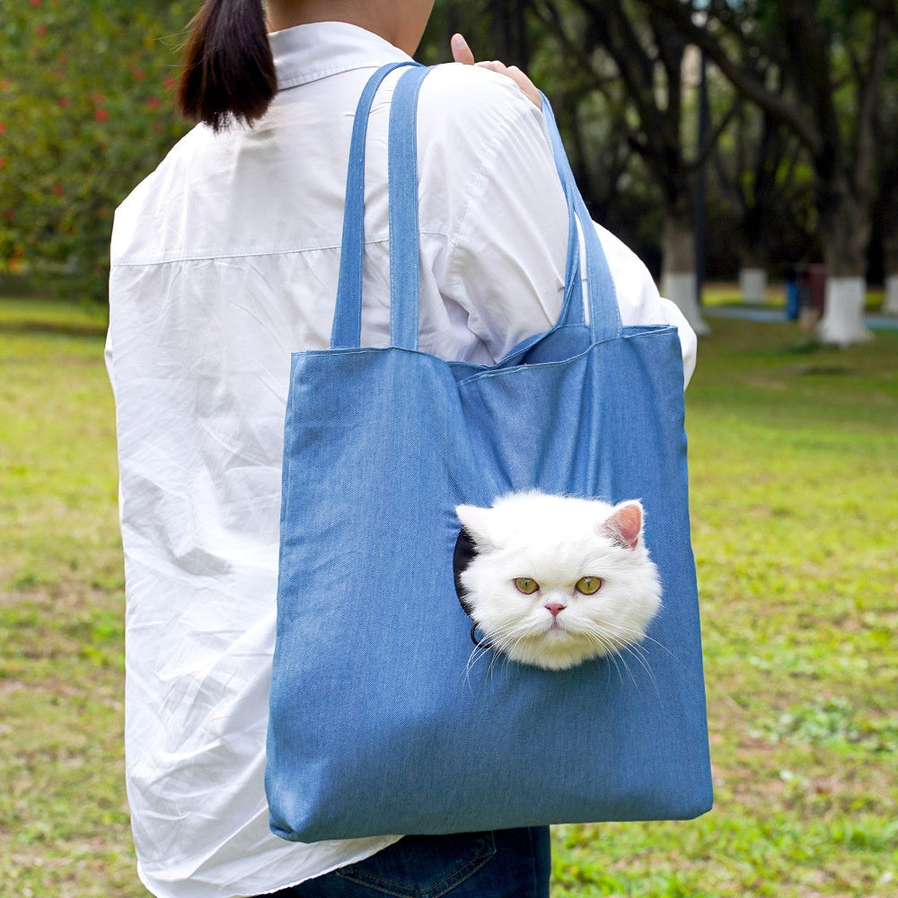 Person holding a blue tote bag with a cat face design outdoors.