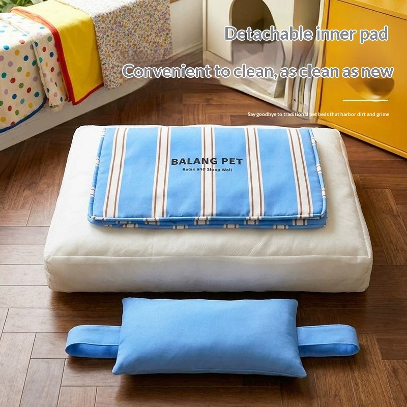 A pet cushion set shown on a wooden floor in a room, featuring a white rectangular cushion with a blue striped detachable inner pad labeled 'BALANG PET' and a separate blue rectangular support pad placed in front. Text on the image describes the detachable inner pad and cleaning convenience.